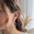 Woman wearing a silver earring with a blurred background of a vase and plants