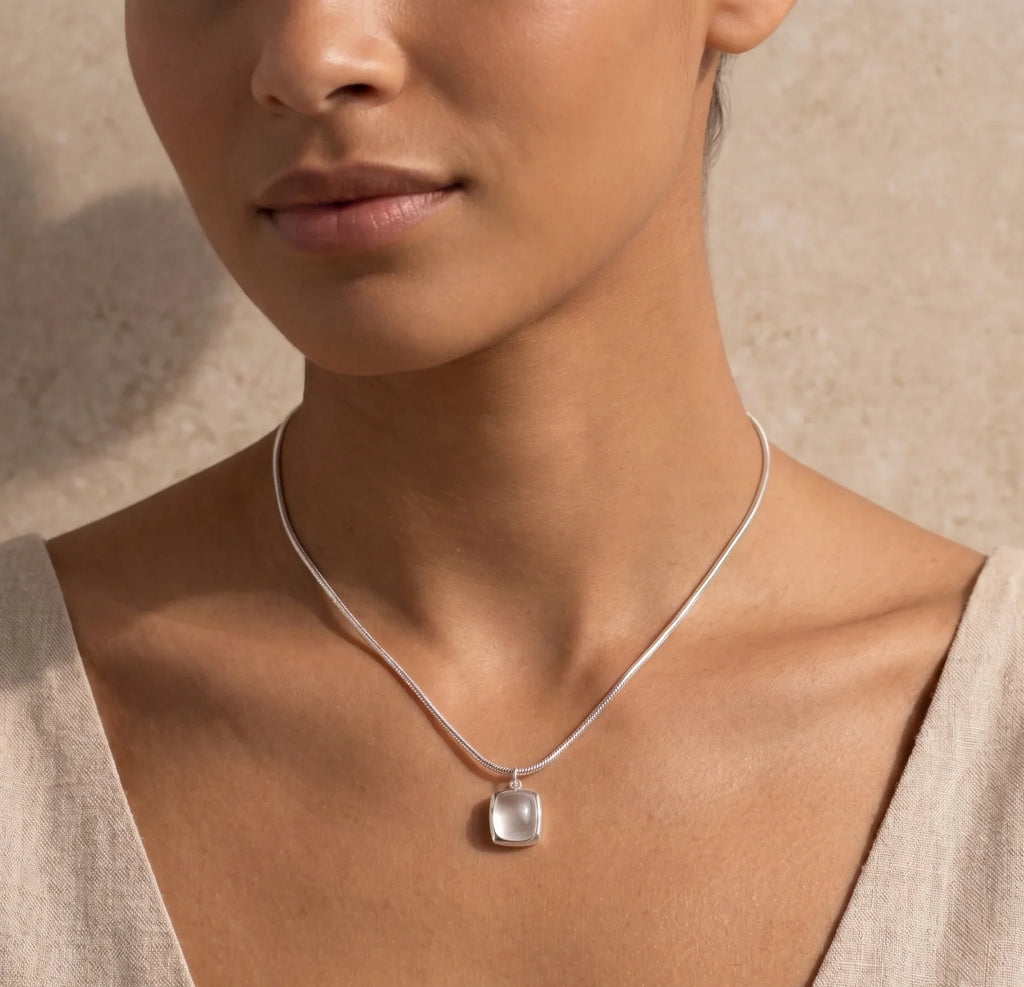 Close-up of a woman wearing a silver necklace with a white agate pendant against a neutral background
