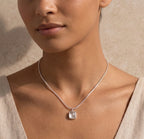Close-up of a woman wearing a silver necklace with a white agate pendant against a neutral background