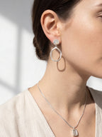 Woman wearing a set of silver drop earrings and pendant necklace with a neutral background